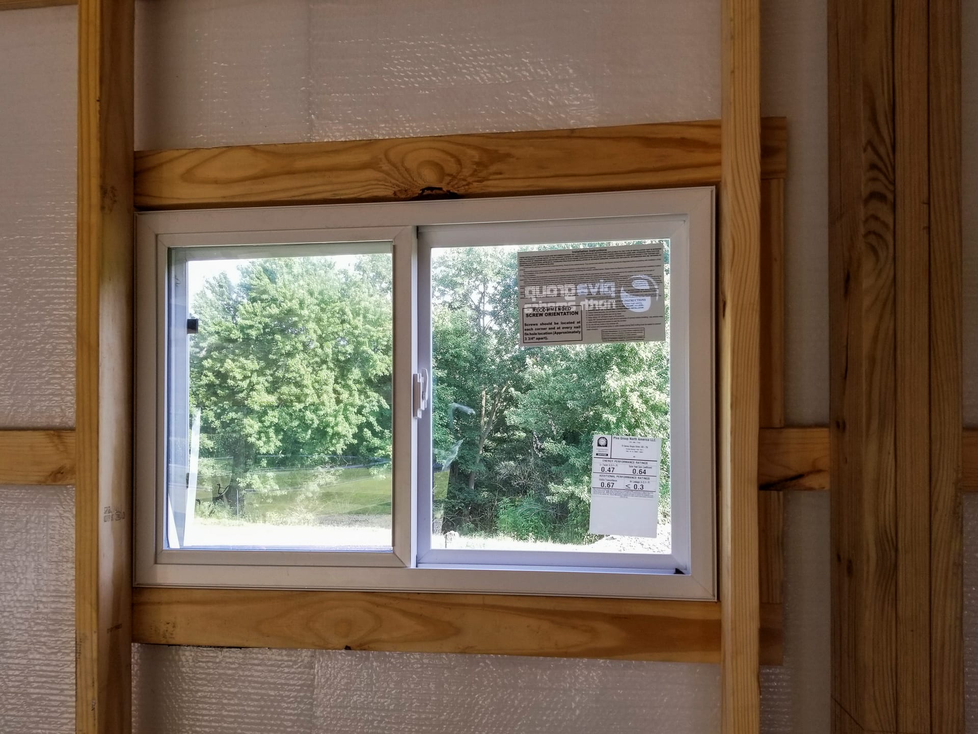 The image features a post-frame construction window from Built-Mor Buildings. The window is set in a wooden frame, suggesting sturdy support, with visible insulation wrapping the surrounding structure. The window is a sliding type and has labels indicatin